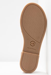 Suela de goma color beige con patrones texturizados en la superficie, que presenta un logo circular y marcas de tamaño. Bordes suaves y forma redondeada.