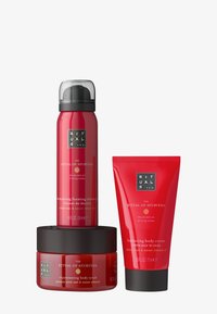 Set di tre prodotti per la cura della pelle rossi: un gel doccia schiumoso, uno scrub per il corpo in un barattolo e una crema per il corpo in tubo, tutti etichettati con accenti neri.