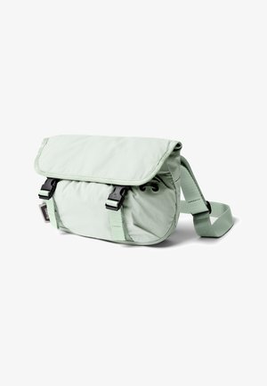 Sac bandoulière vert clair avec sangle ajustable, rabat avant sécurisé par deux boucles en plastique noir, et une petite étiquette de marque sur le côté.