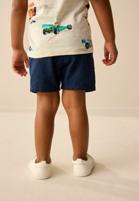 Barntröja med färgglada bilgrafiker, tillsammans med marinblå shorts. Vita sneakers fulländar outfiten, sedd bakifrån.