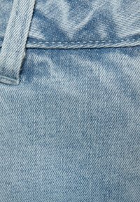 Tissu en denim bleu clair avec une texture lisse, affichant un léger motif décoloré, des coutures visibles et sans matériel ou accents proéminents.