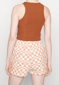 Brązowy prążkowany top na ramiączkach w połączeniu z białymi szortami ozdobionymi pomarańczową kratką i kwiatowymi akcentami. Szorty mają elastyczną talię.