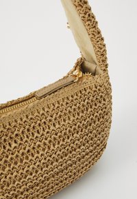 Sac en paille tressée couleur beige, avec une surface texturée, une fermeture zippée et une doublure intérieure contrastante. Inclus : des accents en métal doré.