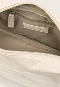 Interno di borsa sintetica beige con texture liscia; presenta una tasca con zip e una fodera tan con etichetta logo. Design semplice, layout funzionale.