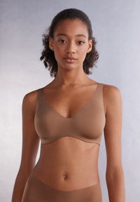 Hnědá bezdrátová podprsenka s výstřihem do V, vyrobená z hladké tkaniny; má široké ramínka a bezšvový design pro pohodlí.