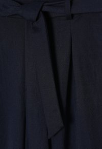 Tessuto blu navy con una texture liscia, dotato di una cintura annodata in vita e pieghe ripiegate. Il design è strutturato e minimalista.