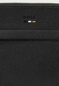 Μαύρο δερμάτινο πορτοφόλι με υφή, διακοσμημένο με φερμουάρ και ανάγλυφο λογότυπο "BOSS", με τρεις μικρές χρωματιστές μπλοκ.