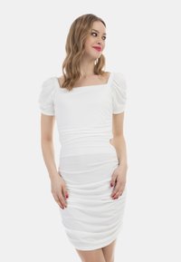 Biała sukienka bodycon z bufiastymi rękawami, kwadratowym dekoltem i detalami drapowanymi po bokach. Gładki materiał; dopasowany krój podkreśla sylwetkę.
