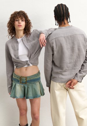 Gray button-up shirt with a knotted front, paired with a pleated denim mini skirt showcasing a faded blue-green gradient. White backdrop.