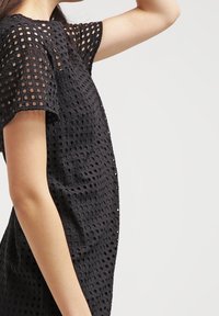 Vestido negro con un diseño de rejilla texturizada y abierta. Mangas cortas y una silueta recta. El material parece ligero y transpirable.