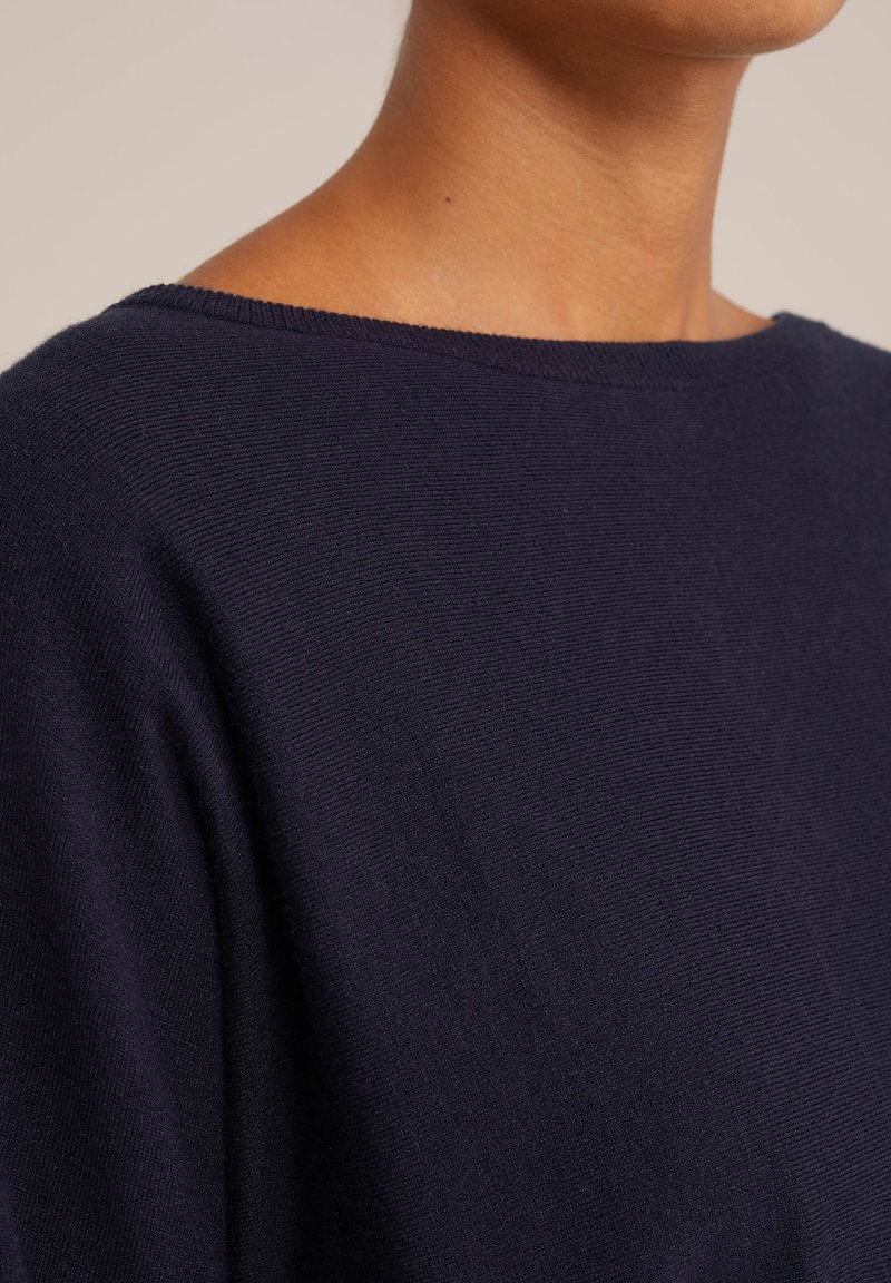 Dunkelblaues Strickoberteil mit weit ausgeschnittener Rundhalslinie, weicher Textur und ohne sichtbare Muster oder Verzierungen. Fokussiert auf Schlichtheit und Komfort.