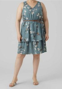 Blomstret kjole i teal stof, med v-hals, ærmeløs design, lagdelt nederdel og en indsnævret talje med en flettet bælte detalje.