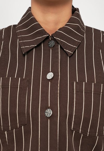 Brown striped shirt featuring a collared neckline, two chest pockets, and textured buttons. The fabric has a canvas-like quality.
