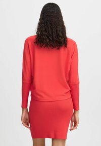 Pull en maille rouge, à coupe décontractée et manches longues, associé à une jupe mini côtelée assortie. Texture douce, détails minimaux.