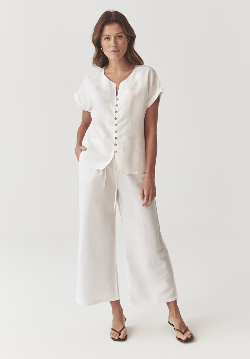 Chemisier en lin blanc à boutons sur le devant avec des manches courtes, associé à un pantalon en lin blanc à jambes larges. Design minimaliste avec une coupe décontractée.