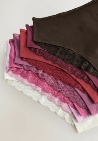 Pile de sept sous-vêtements féminins ornés de dentelle dans des nuances de brun, rouge, rose et blanc, disposés sur un fond neutre.