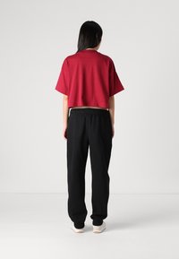 Korte, cropped rode T-shirt met korte mouwen in combinatie met zwarte trainingsbroek; het T-shirt heeft een ontspannen pasvorm en de broek heeft een elastische tailleband en boorden.