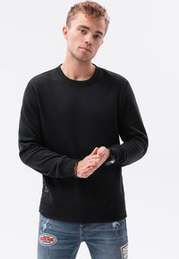 Sort sweatshirt lavet af blødt stof, med rund halsudskæring, lange ærmer, ribbede manchetter og en løs pasform. Subtil logo-detalje ved kanten.