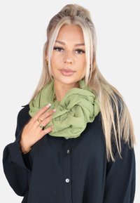 Green textured infinity scarf worn over a dark shirt. Soft, crinkled fabric with a layered appearance, featuring a subtle pattern.