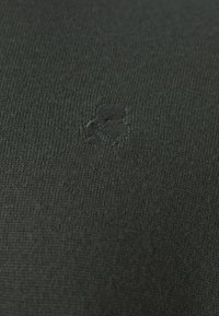 Dunkelgrüner Strickstoff mit einem dezent geprägten Logo in passender Farbe, das eine glatte Textur und ein minimalistisches Design bietet.