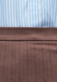 Svetlo modra prugasta srajca nad rjavo tkanino spodaj, z gladko teksturo in vertikalnimi črtami. Nema izrazite strojne opreme ali dodatkov.