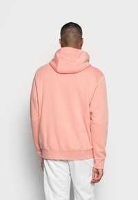 Ljusrosa hoodie med en rymlig huva, ribbad ärmslut och midja. Tyget ser mjukt och texturerat ut, lämpligt för avslappnad klädsel.