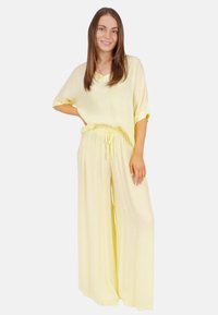 Hellgelbes Zweiteiler-Outfit mit einem locker sitzenden Oberteil und einer weit geschnittenen Hose. Der Stoff wirkt weich mit einer dezenten Textur und einem Kordelzugbund.