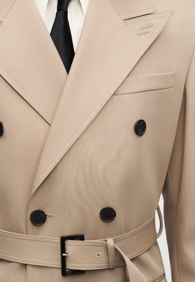 Beiger doppelt geknöpfter Trenchcoat mit Gürtel, schwarzen Knöpfen, spitzen Revers und einer linken Brusttasche. Aus texturiertem Stoff und maßgeschneidertem Design.