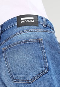 Siniset farkut, joissa on musta DRDENIM -merkki vyötäröllä, takatasku ja klassiset ompeluyksityiskohdat.