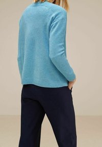 Ljusblå stickad tröja med ribbade muddar och fåll, bärs över mörka ribbade byxor. Texturen verkar mjuk och bekväm.