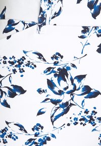 Bílá látka s modrým květinovým vzorem s detailními květy a stonky. Design zahrnuje různé odstíny modré a složité textury.