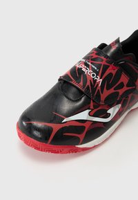 Scarpe da calcio nere e rosse con una parte superiore in tessuto sintetico testurizzato, dotate di una fascia in velcro e di un logo bianco sul lato. Suola in gomma rossa.