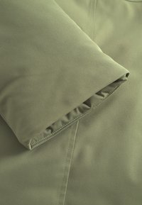 Olive green jacket fabric with a smooth texture, featuring a folded cuff and neat stitching along the edges.