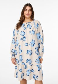 Robe à manches longues présentant une base beige et un motif floral bleu. Le design comprend un col froncé et un ourlet à volants pour plus de détails.