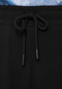 Zwarte sweatpants met een elastische tailleband, voorzien van een trekkoord met zwarte aglets. Glad materiaal met een matte afwerking.