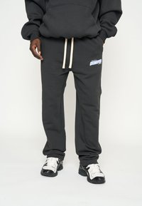 Zwarte katoenen sweatpants met een beige trekkoord, met een blauwe "MULTIPLY" logo op de linker dij en een relaxte pasvorm.