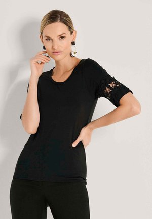 Zwart T-shirt met korte mouwen en bloemrijke kantaccenten aan de mouwzomen. Zacht materiaal en een ronde hals.