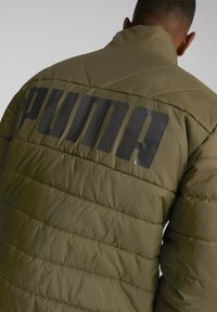 Veste matelassée vert olive avec texture matelassée diagonale. Présente un grand logo PUMA noir au dos et un col montant pour plus de chaleur.