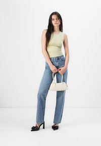 Mouwloos lichtgroen topje, hoogoplopende blauwe jeans, zwarte hakken met strikken, en een kleine witte handtas.