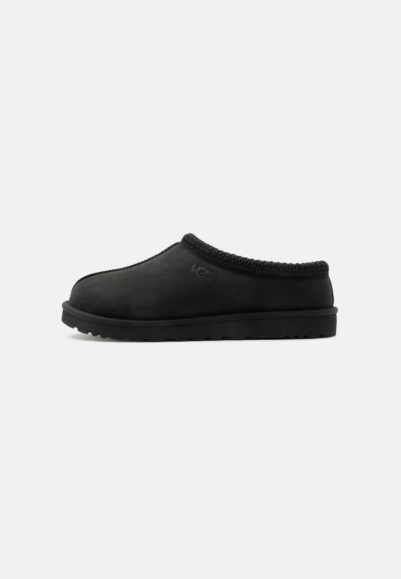 Chausson noir à enfiler UGG avec une semelle souple et une bordure tricotée autour du col, vue de côté sur fond blanc.