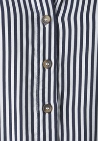 Camisa de rayas horizontales en azul marino y blanco con un cierre de botones en la parte delantera, botones redondos y brillantes, y una textura de tela suave.