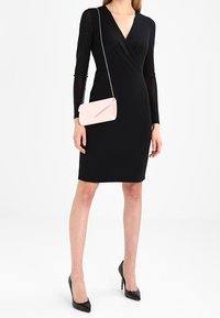 Czarna sukienka z długim rękawem o kopertowym fasonie, dekoltem w kształcie litery V i dopasowanym kroju. Do kompletu mała różowa kopertówka oraz czarne szpilki.