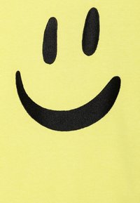 Gul farge har et stort svart smilefjes-design, med runde øyne og et bredt, buet smil, som fremhever en enkel og leken estetikk.