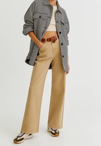 Zwart-wit geruite oversized jas, beige brede broekspijpen, bruine riem en meerkleurige sneakers. Eenvoudige, gestructureerde stoffen.