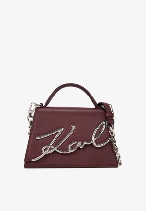 Bordeaux nahka käsilaukku rakenteellisella muotoilulla, jossa on hopeaketju ja logo korostus edessä. Kompakti ja kulmikas muoto.