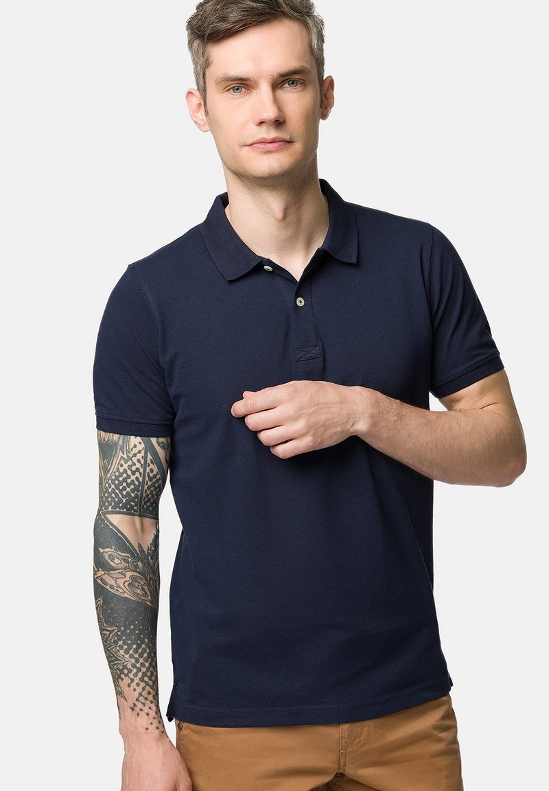 Granatowa koszulka polo z miękkiego materiału, klasycznym kołnierzykiem, zapięciem na dwa guziki i krótkimi rękawami. Posiada subtelną strukturę.