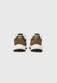 Pár hnedej a čiernej sneakers s bielymi podrážkami, z pohľadu zozadu, s logom "A | X" na pätnom pätku.