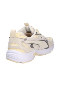 Beige athletic shoe with a textured upper, grey accents, padded collar, and a chunky white sole. Features branding on the side and pull tab.
