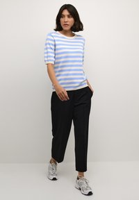 Blå og creme-stribet kortærmet sweater parret med løse sorte bukser og grå sneakers. Blød tekstur, afslappet pasform og afslappet stil.