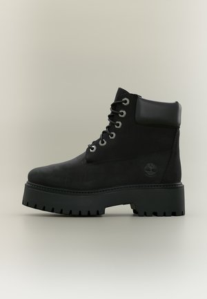 Bottine noire en cuir à lacets avec semelle épaisse crantée et col matelassé, logo embossé sur le côté au niveau du talon.